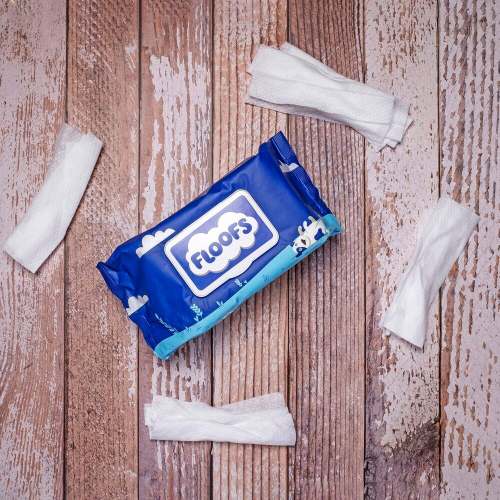 A Floofs wipes packet surrounded with loose wipes on a rustic wooden surface
