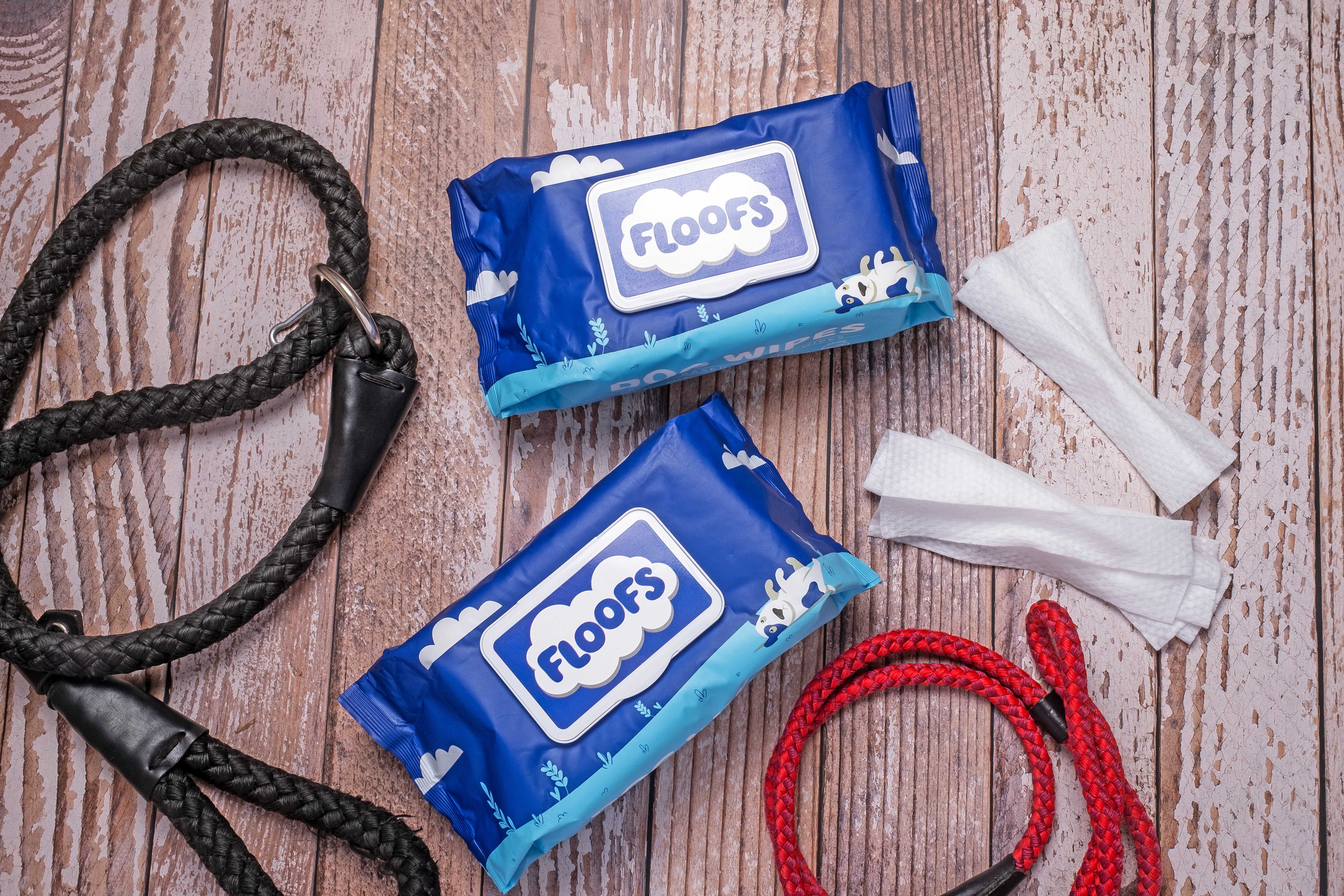 Floofs Pet wipes on a wooden surface surrounded by dog leads and loose wipes